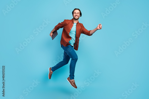 Full lengh photo of funky brunet millennial guy run with laptop wear eyewear shirt trousers footwear isolated on blue background photo