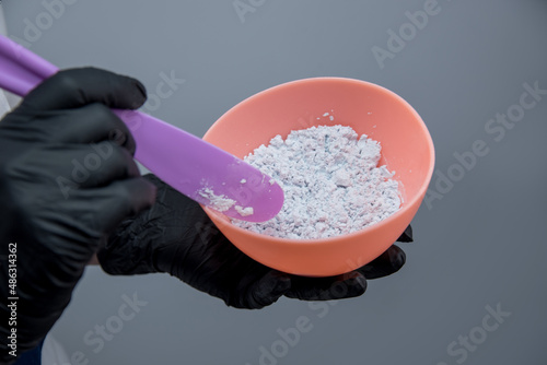 female hands in medical gloves hold a bowl of white powder