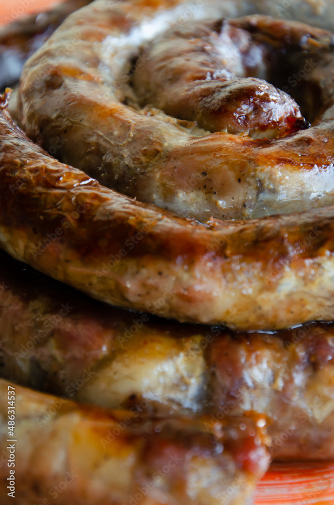 Tasty delicious fried homemade sausage ring lies on plate. Juicy sausage grill for the holiday table. Fatty junk food cooked from meat.