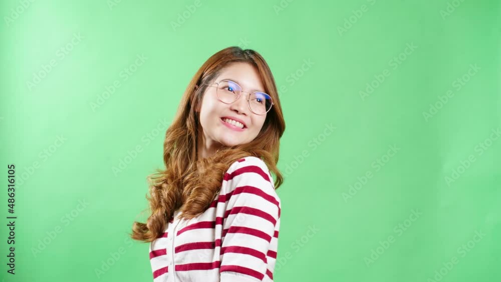 Cheerful young Asian woman with eyeglasses raising hands up, shaking and having fist pump from happiness, smiling woman face, green screen background.