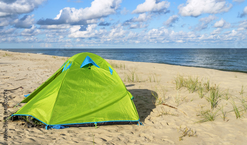 Green tent on the sea sand. Hiking tent on the beach. Baltic coast quiet sea.