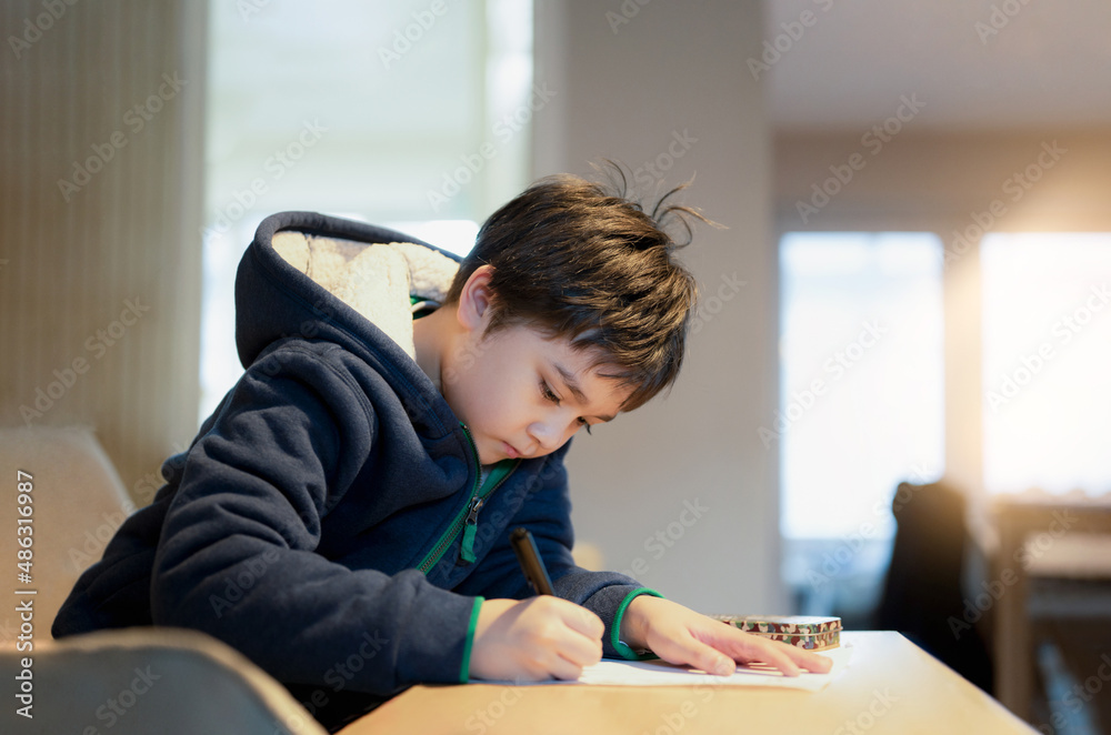 School kid using black pen drawing or writing the letter on paper, Young boy doing homework, Child with pen writing notes in paper sheet during the lesson.Cute pupil doing test, Homeschooling concept School kid using black pen drawing or writing the letter on paper, Young boy doing homework, Child with pen writing notes in paper sheet during the lesson.Cute pupil doing test, Homeschooling concept