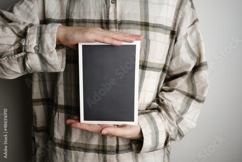 The girl is holding a book with a black cover and a white frame. Place for text and advertising. Book or stylish notebook close-up