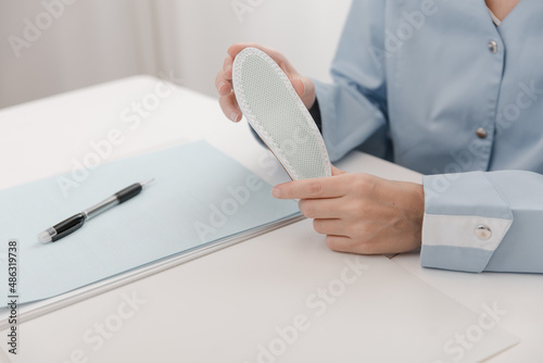 Doctor holding an insole while sitting at a table. Orthopedist tests the medical device. Orthopedic insoles. Foot care. Flat Feet Correction. Treatment and prevention of flat feet and foot diseases.