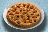 Apulian focaccia, typical italian Bari pizza with cherry tomatoes and black olives on top. In white plate on light blue wooden table