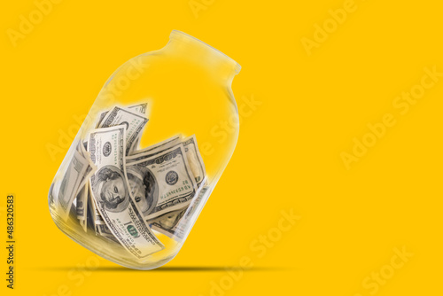 Many 100 US dollars bank notes in a glass jar isolated on yellow background