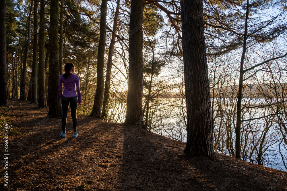 Female jogger standing in forest and looking at lake