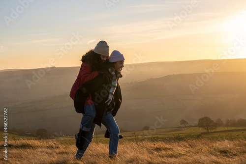 Young woman giving friend piggyback ride in rural landscape