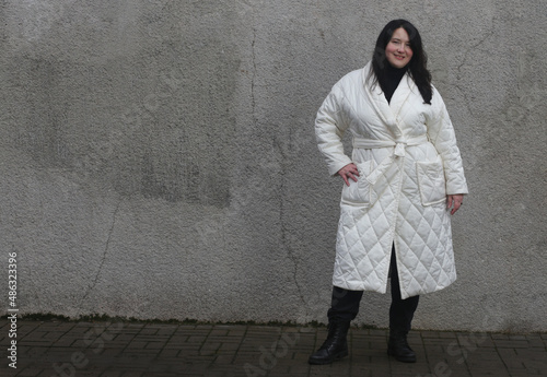 A beautiful brunette plus size in a white coat looks at the camera.