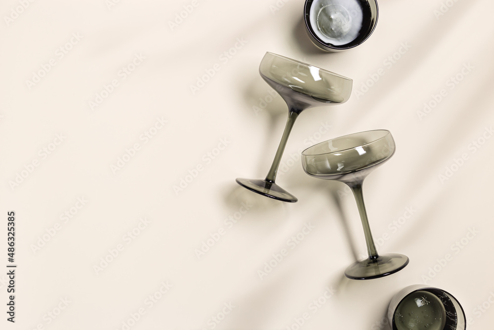 Champagne glass made of tinted grey glass on beige table background. Minimal fashion drink concept. Trendy wine glasses, vintage colored glass. Creative flat lay, top view pattern. Champagne glass made of tinted grey glass on beige table background. Minimal fashion drink concept. Trendy wine glasses, vintage colored glass. Creative flat lay, top view pattern.