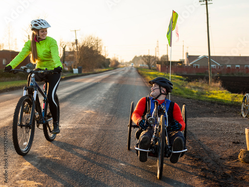 Woman riding bike and disabled man riding handcycle on country road photo