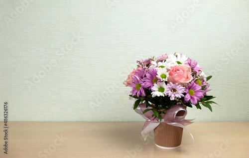 A beautiful bouquet of flowers in a vase with a bow is on the table. Place for text