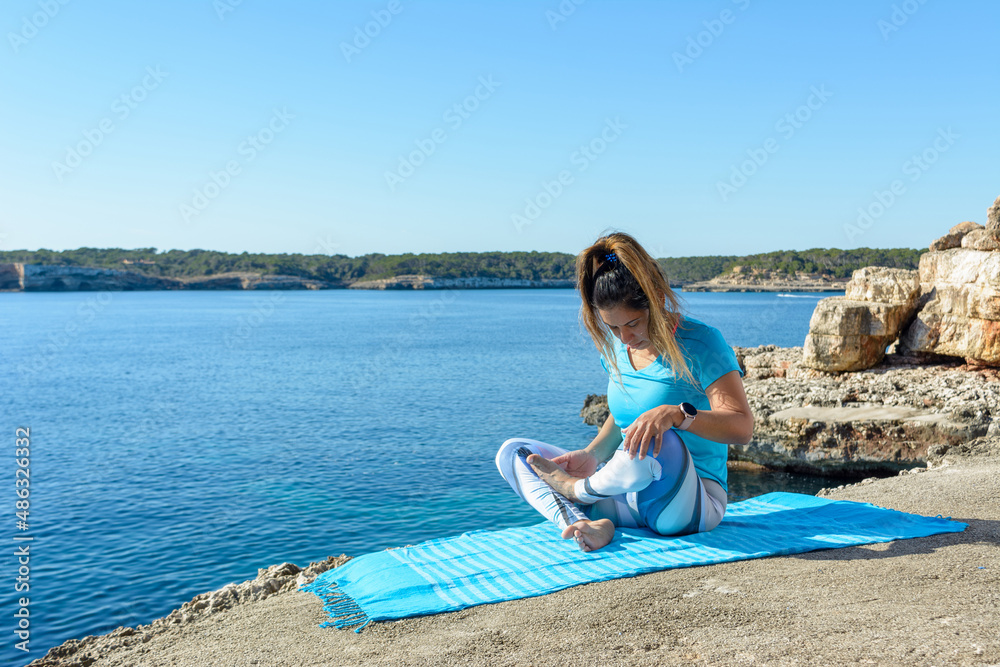 middle-aged fitness woman outdoors in front of the sea does yoga stretching exercises