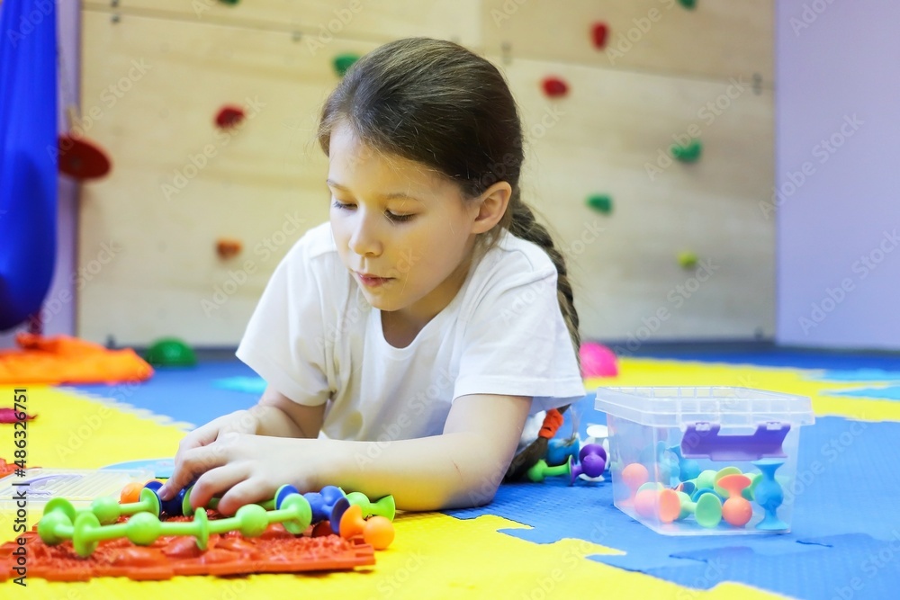 a child a girl on the floor of a children's rehabilitation center for correction collects a chain of viruses from a toy. the concept of lifestyle a child a girl on the floor of a children's rehabilitation center for correction collects a chain of viruses from a toy. the concept of lifestyle