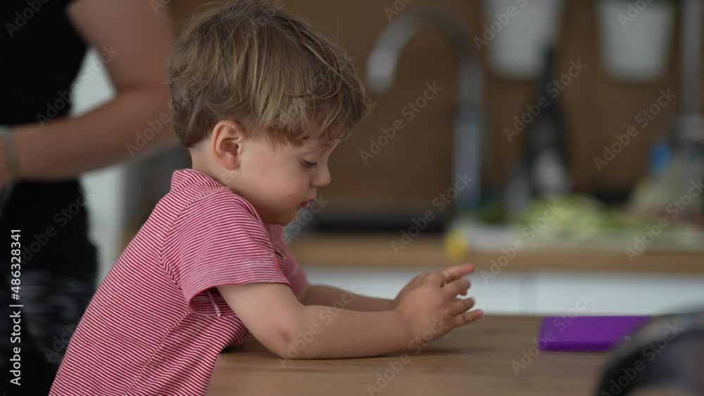 Bored little boy at home trying to reach for object at kitchen table Bored little boy at home trying to reach for object at kitchen table