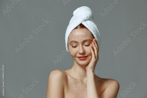 Beautiful young girl with towel on head, naked shoulders, touches soft healthy skin. Beauty skincare cosmetics ad