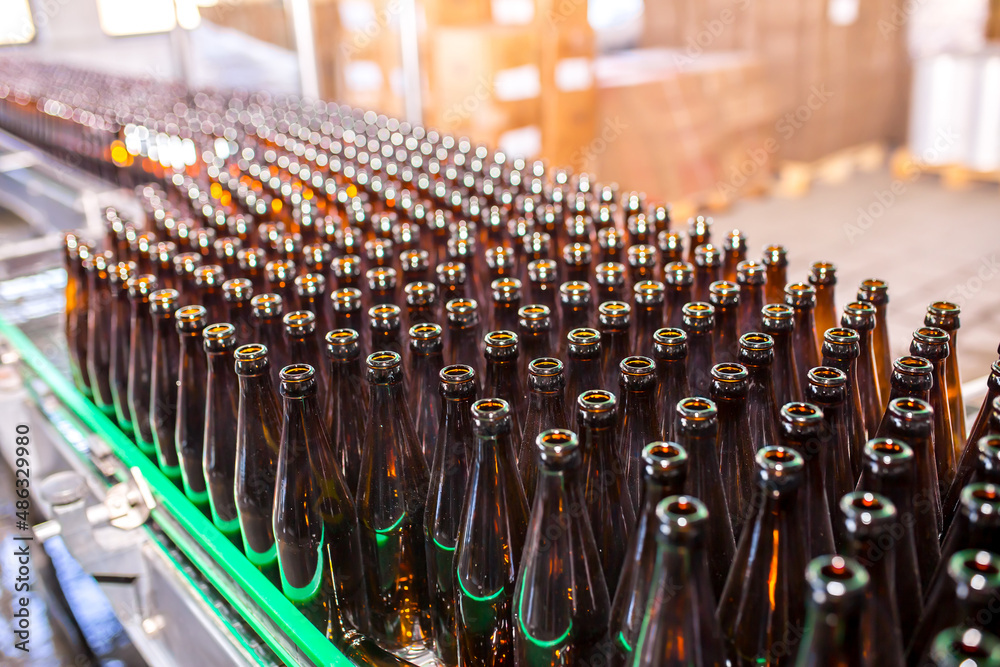 Brewery factory spilling beer into glass bottles on conveyor lines. Industrial work, automated production of food and drinks. Glass products. Bottles for drinks. Technological work at the factory.