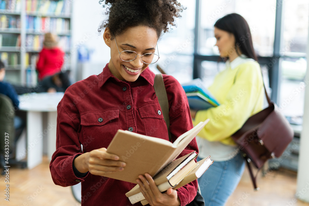 Smiling confident teen girl college student looking at the book while reading. Happy multiracial woman wearing glasses posing in library classroom Smiling confident teen girl college student looking at the book while reading. Happy multiracial woman wearing glasses posing in library classroom