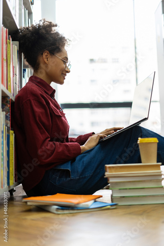 Side view of the focused multiracial school girl studying with laptop while preparing for test exam or doing homework. Teenage student learning assignment making notes. Teen education concept