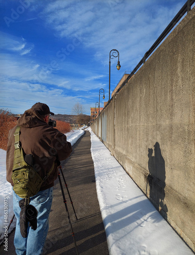 A male photographer with his camera and tripod takes photos while walking the Chenango River Walk in Binghamton in Upstate NY.   photo