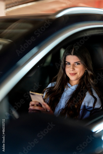 Attractive young woman inside a car smiling looking at smartphone