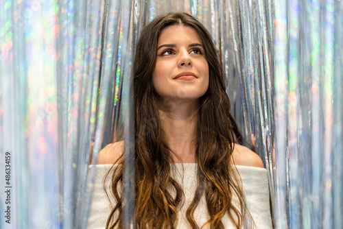 Portrait of an attractive and elegant young woman looking at the camera between a curtain of glitter and silver and colored reflections