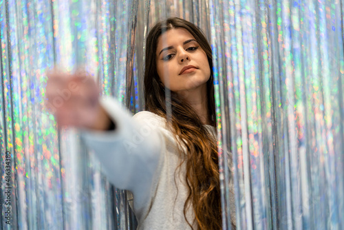 Portrait of an attractive and elegant young woman looking at the camera between a curtain of glitter and silver and colored reflections