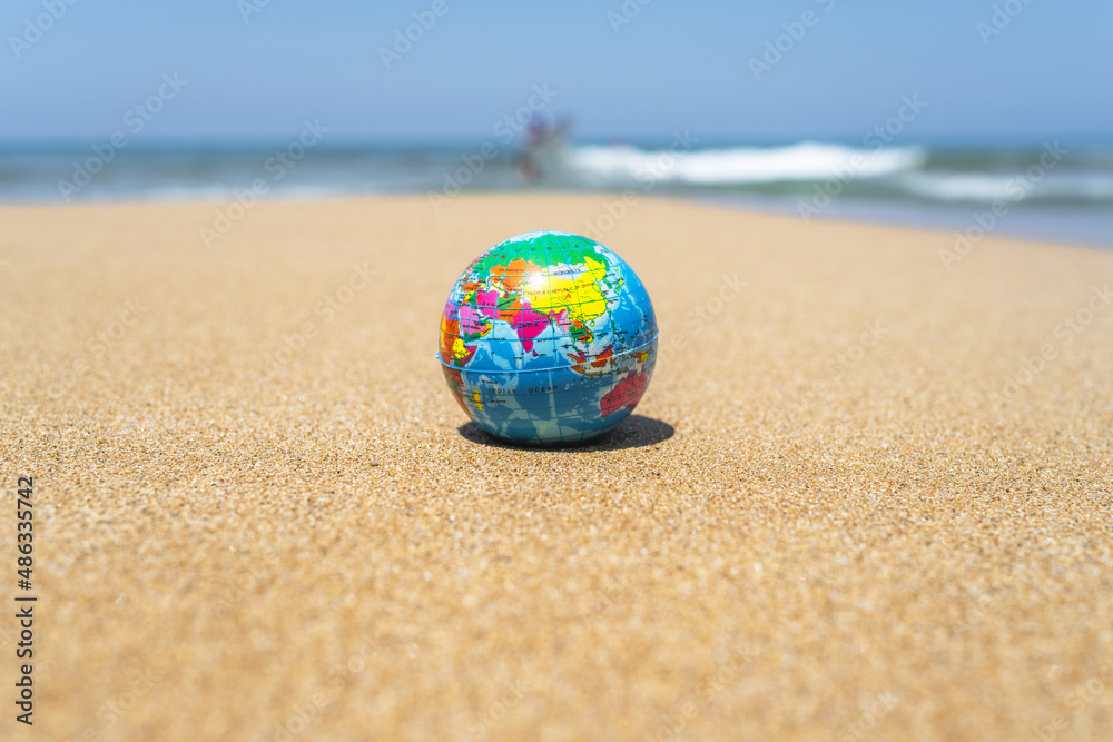 Toy globe on the sand of beach with sea wave background. World travel concept.
