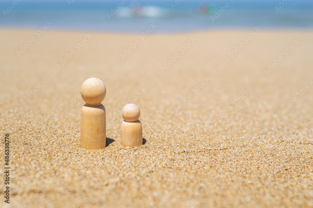 Wooden two figures of people on the sand of beach with sea view. Concept of happy children on holiday.