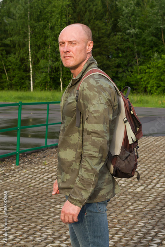 A sporty man in a military jacket and with a backpack. Vertical photo.