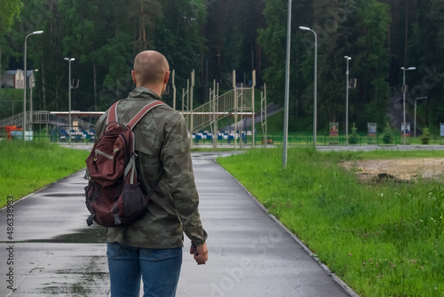 A sporty man in a military jacket and with a backpack. View from the back. Empty space for the text.