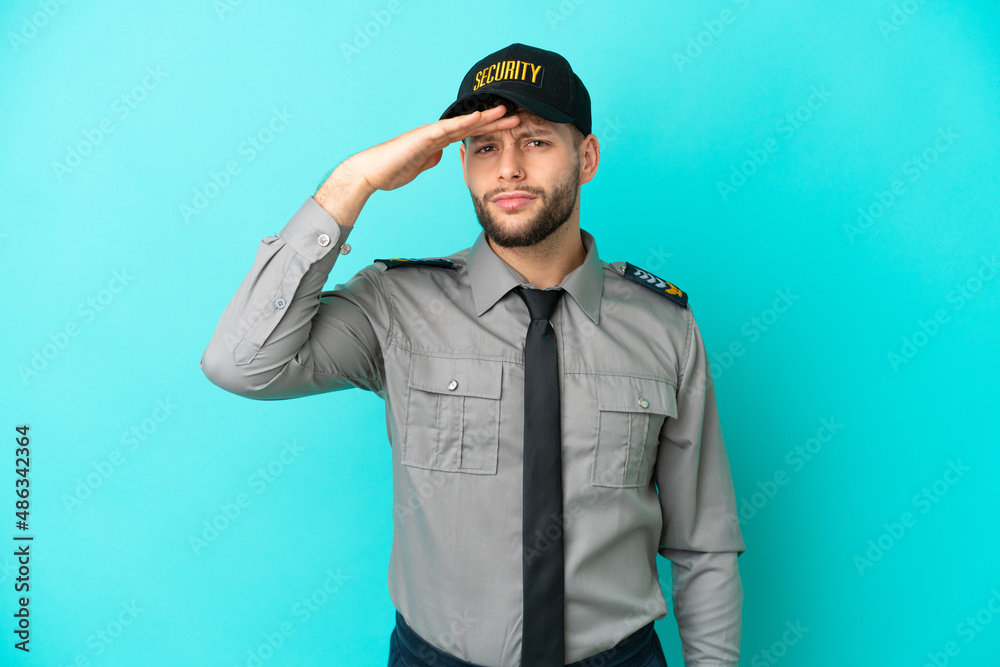 Young security man isolated on blue background looking far away with hand to look something Young security man isolated on blue background looking far away with hand to look something