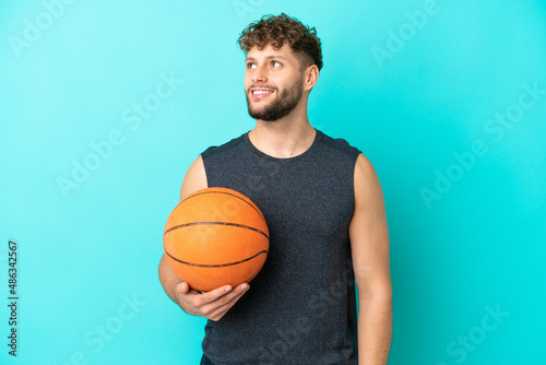 Handsome young man playing basketball isolated on blue background thinking an idea while looking up
