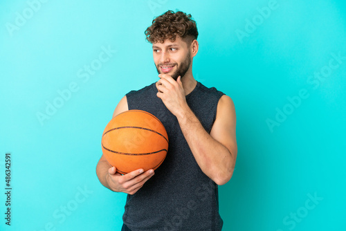 Handsome young man playing basketball isolated on blue background looking to the side and smiling