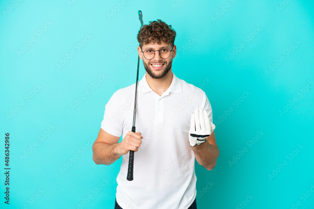 Young handsome caucasian man isolated on blue background playing golf and doing coming gesture
