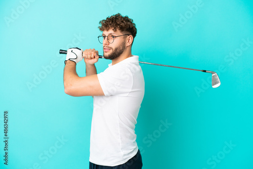 Young handsome caucasian man isolated on blue background playing golf