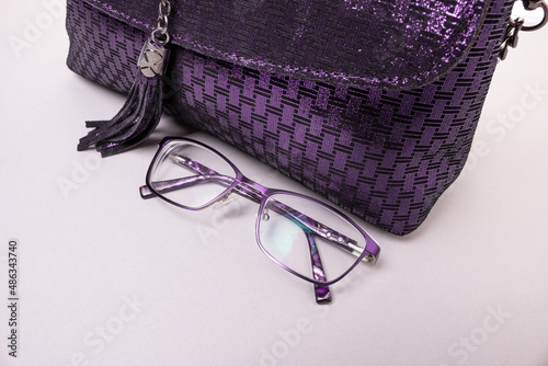 Purple suede bag and purple-rimmed glasses. Beige background