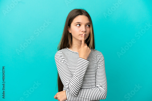 Little girl over isolated blue background having doubts while looking up