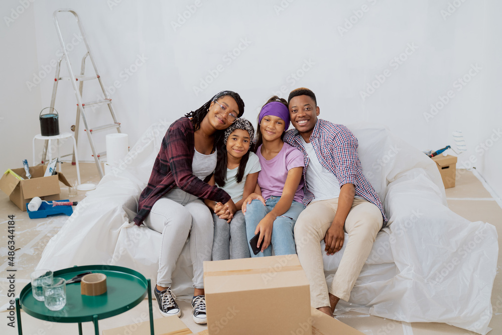 Portrait of a happy smiling loving family sitting on a couch during an apartment renovation. Young parents and two daughters looking for camera Portrait of a happy smiling loving family sitting on a couch during an apartment renovation. Young parents and two daughters looking for camera