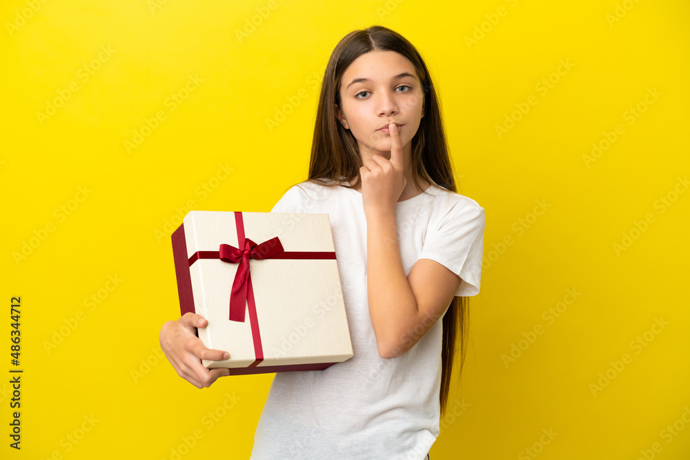 Little girl holding a gift over isolated yellow background having doubts while looking up Little girl holding a gift over isolated yellow background having doubts while looking up