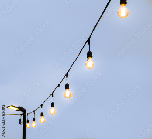 Close up of anging antique edison style filament light bulbs on wire with blurry background. Industrial pendant glowing lamps near cafe at street, isolated.