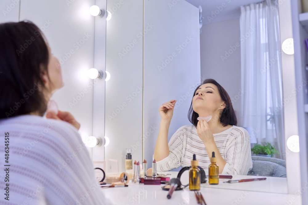 Middle age facial skin care woman doing facial massage with gua sha scraper. Middle age facial skin care woman doing facial massage with gua sha scraper.
