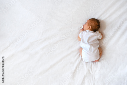 Top view of cute adorable newborn baby wearing white body sleeping on stomach