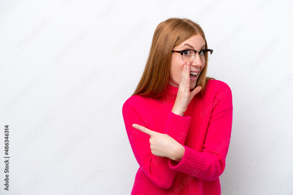 Young redhead woman isolated on white background pointing to the side to present a product and whispering something Young redhead woman isolated on white background pointing to the side to present a product and whispering something