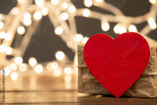 Valentine s Day greetings concept. Little red wooden heart close up  party lights bokeh on background. Valentines greeting card.