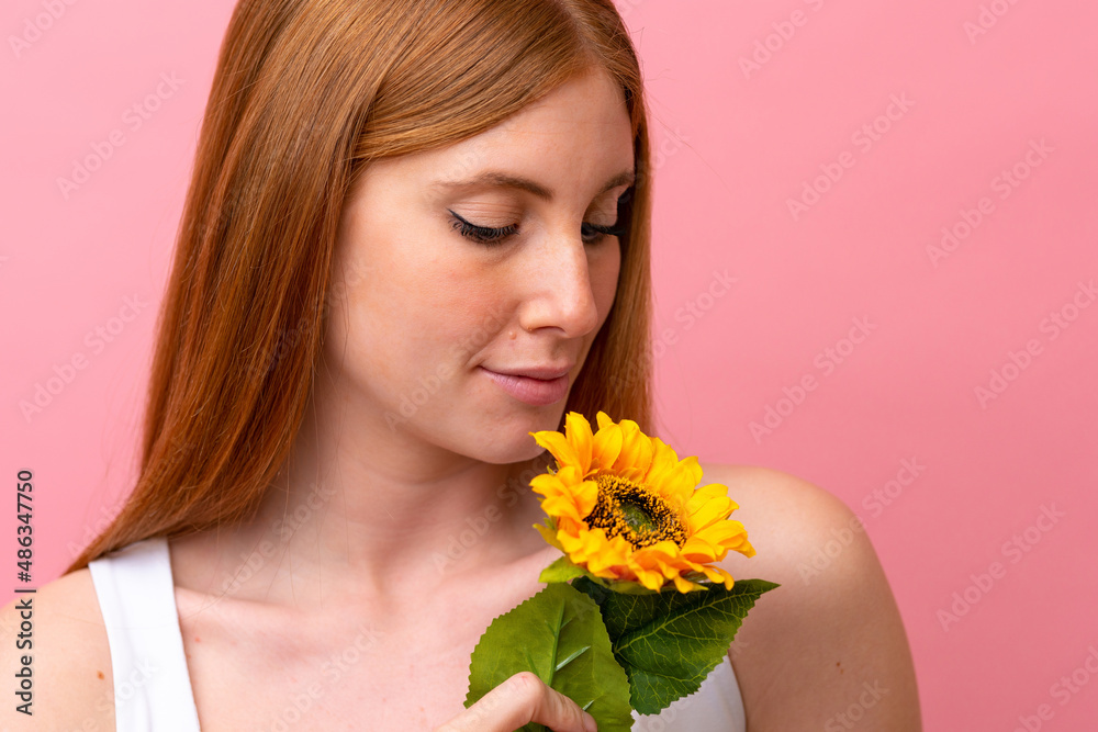 Young redhead woman isolated on pink background holding a sunflower. Close up portrait