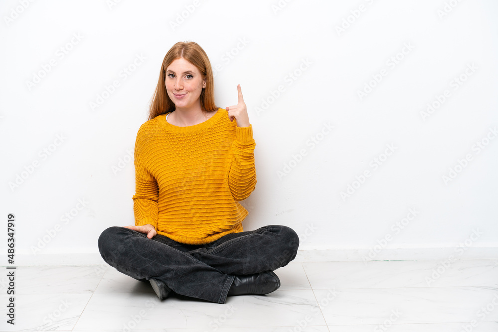 Young redhead woman sitting on the floor isolated on white background pointing with the index finger a great idea Young redhead woman sitting on the floor isolated on white background pointing with the index finger a great idea