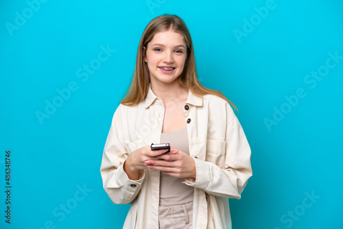Teenager Russian girl isolated on blue background sending a message with the mobile