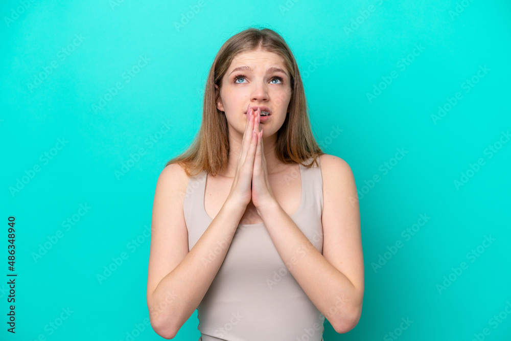 Teenager Russian girl isolated on blue background keeps palm together. Person asks for something Teenager Russian girl isolated on blue background keeps palm together. Person asks for something