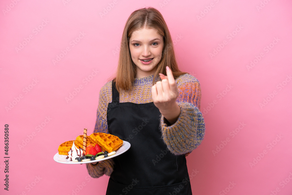 Teenager Russian girl holding a waffles isolated on pink background doing coming gesture